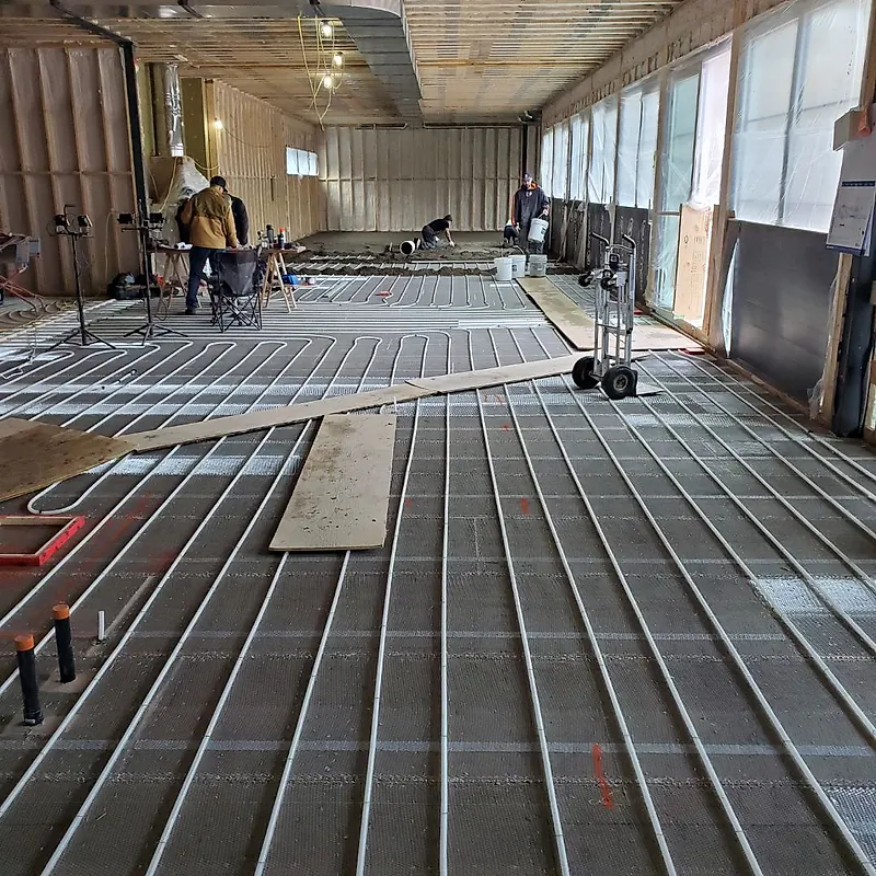 Large open framed building with heating tubes laid in rows on mesh, walk boards, buckets and workers mixing at the far end