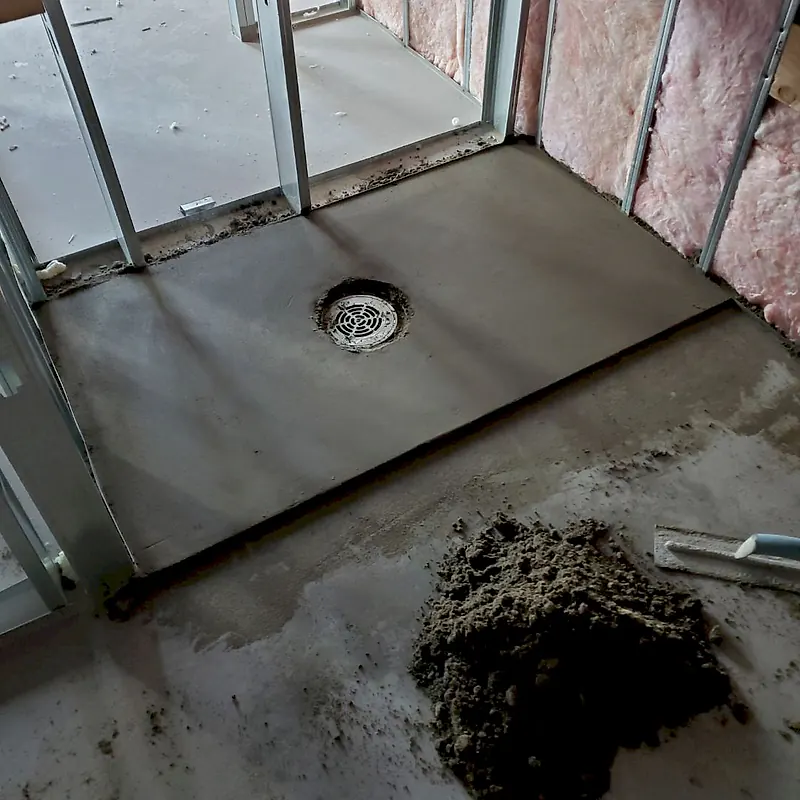 Dry pack shower pan between steel studs with a round chrome drain grate, a pile of mortar and a float in front